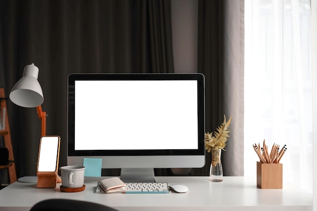 Mock up computer and smart phone with white screen on white table at comfortable home office.