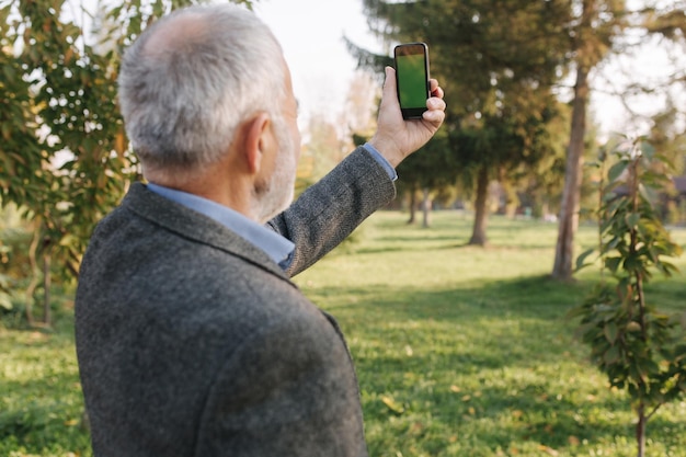 Mock up of elderly man using phone outside Green screen Back view of man holding phone at harm's