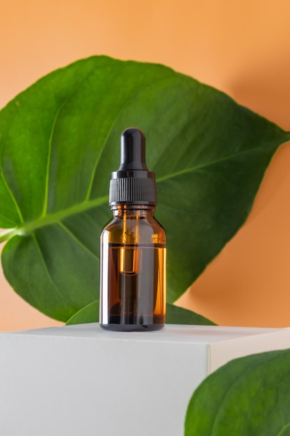 Mock up glass dropper bottle on a white podium on a beige background with leaves Scin care concept