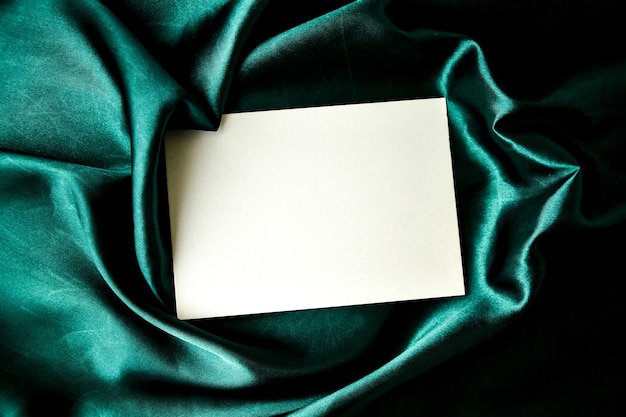 モックアップ挨拶の入力背景緑色の絹の布、白い紙グリーティングカードのフラットレイ構成季節の画像コピースペース