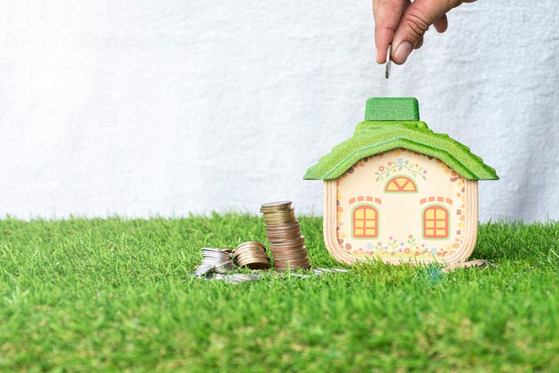 Mock up house with coins stack on grass floor and hand putting money coin