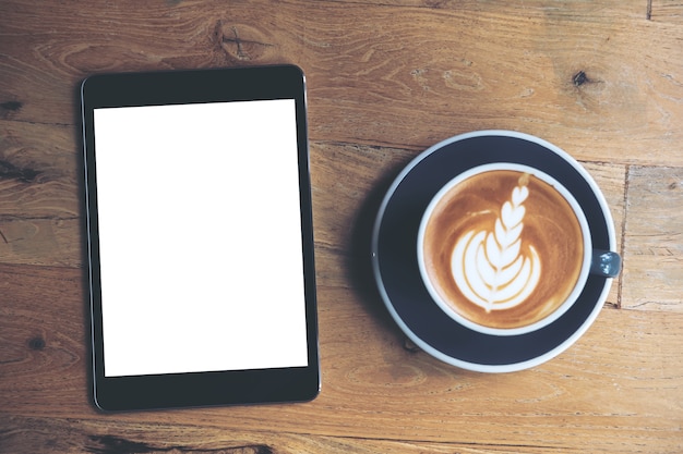 Mock up image of black tablet with white blank screen and coffee cup on vintage wooden table