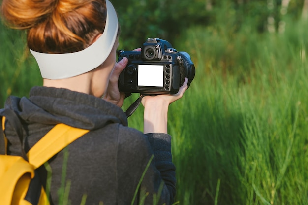 Mock-up in de handen van een meisje met een reflexcamera in het bos. tegen de achtergrond van prachtig groen.