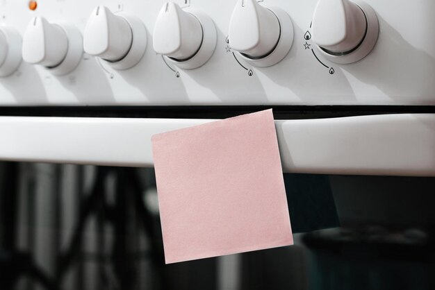 Mock up memo sticker with blank space pasted on gas stove panel in kitchen selective focus on sheet