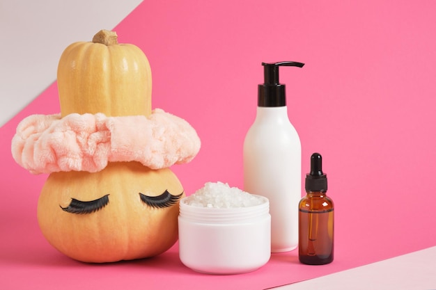 Mock up set of cosmetic containers and pumpkin with headband and false eyelashes on pink background