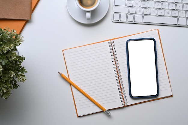 Photo mock up smart phone with blank screen and empty notebook on white office desk.