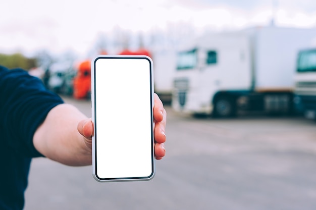Mock up a smartphone in the hand of a man. Against the background of red trucks. Logistics concept.