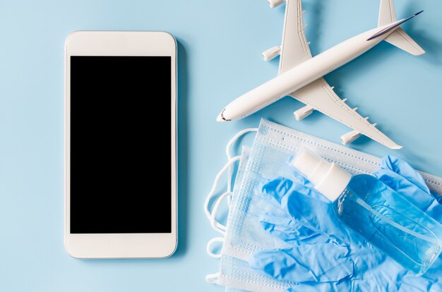 Mock up of smartphone with airplane model, face mask, disposable gloves and hand sanitizer spray