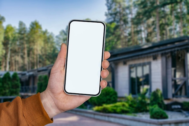 Mock up of a smartphone with white screen in hands, against the background of modern houses.