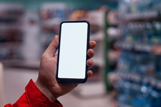 Mock-up of a smartphone with a white screen in the hands of a man. Phone on the space of showcases in the store.