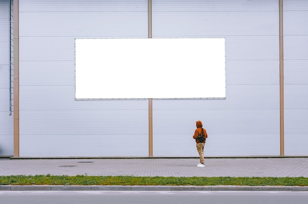 Foto un mock-up di un cartellone stradale contro un muro grigio con un uomo che cammina.