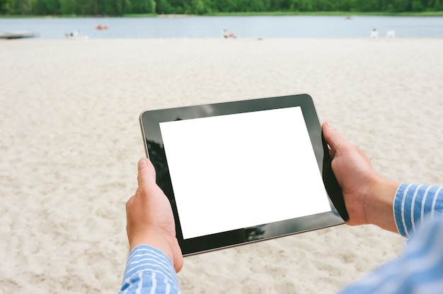 남자의 손에 태블릿을 비웃습니다. 해변과 호수를 배경으로.