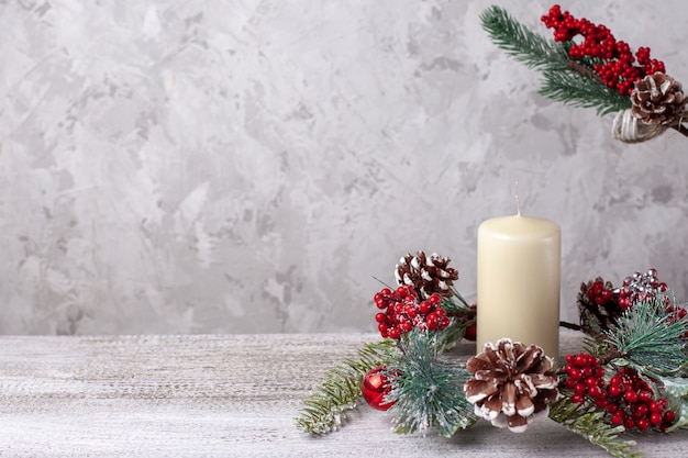 Mock up of two beige vanilla thick Christmas candles and wreath of cones, red berries and  branch.