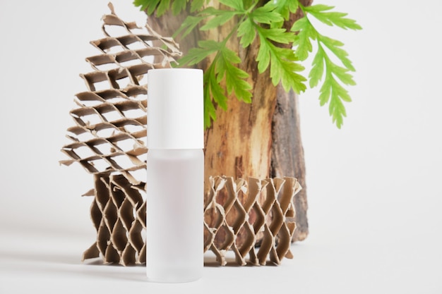 Mock up white blank perfume bottle, green fresh leaves and wooden log on gray background. natural cosmetic concept, creative background for your product