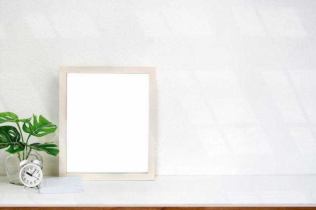 Mock up white wooden frame with blank page and houseplant on white table 