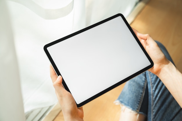 Mock up of woman hand holding digital tablet and touching blank screen.