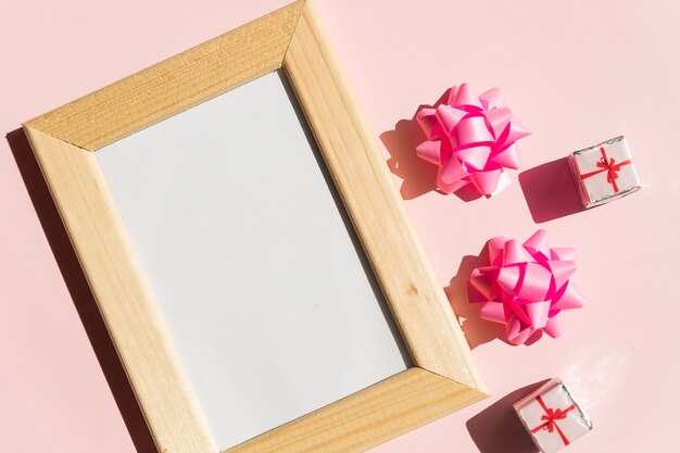 Mock-up del telaio in legno con copia spazio per poster e scatole regalo, fiocco in raso rosa su sfondo rosa. festa della mamma, festa della donna o altra carta vacanze adatta, cornice per foto con spazio di copia per il testo