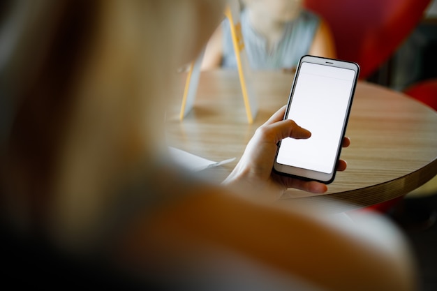 Mockup afbeelding van de handen van de vrouw met witte mobiele telefoon met leeg scherm in café.