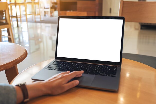 Mockup-afbeelding van een hand die aanraakt op het touchpad van een laptopcomputer met een leeg wit desktopscherm op houten tafel