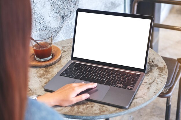 Mockup-afbeelding van een hand die aanraakt op het touchpad van een laptopcomputer met een leeg wit desktopscherm op tafel