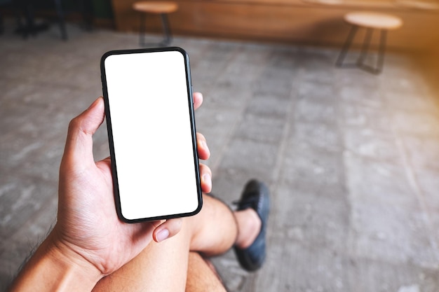 Mockup-afbeelding van een hand die een mobiele telefoon vasthoudt en toont met een leeg wit scherm in café