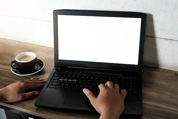 Mockup-afbeelding van een man die een laptop gebruikt en gebruikt met een leeg wit scherm met een koffiekopje op houten tafel