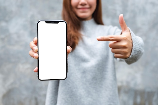 Mockup-afbeelding van een mooie vrouw die een mobiele telefoon met een leeg wit scherm toont en wijst