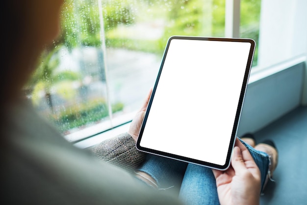 Mockup-afbeelding van een vrouw die een digitale tablet vasthoudt en gebruikt met een leeg wit bureaubladscherm terwijl ze op de grond zit