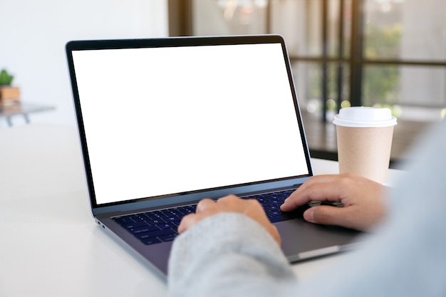 Mockup-afbeelding van een vrouw die een laptop gebruikt en typt met een leeg wit desktopscherm met een koffiekopje op tafel