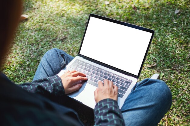 Mockup-afbeelding van een vrouw die een laptop gebruikt en typt met een leeg wit scherm, zittend in de buitenlucht