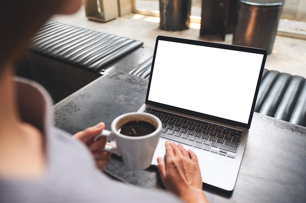 Mockup-afbeelding van een vrouw die een laptop-touchpad gebruikt en aanraakt met een leeg wit bureaubladscherm terwijl ze koffie drinkt