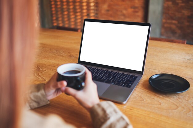 Mockup-afbeelding van een vrouw die een laptopcomputer gebruikt en bekijkt met een leeg wit desktopscherm terwijl ze koffie drinkt