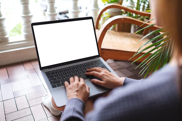 Mockup-afbeelding van een vrouw die een laptopcomputer gebruikt en eraan werkt met een leeg wit bureaubladscherm terwijl ze thuis op het balkon zit