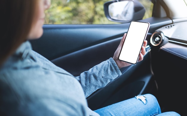 Mockup-afbeelding van een vrouw die een mobiele telefoon vasthoudt en gebruikt met een leeg scherm in de auto