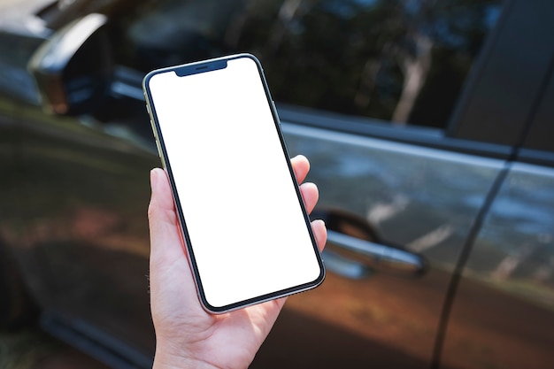 Mockup-afbeelding van een vrouw die een mobiele telefoon vasthoudt en gebruikt met een leeg scherm met een auto op de achtergrond