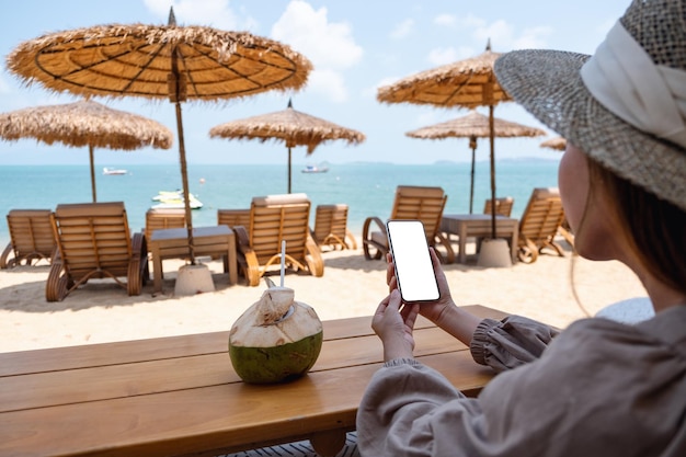 Mockup-afbeelding van een vrouw die een mobiele telefoon vasthoudt met een leeg desktopscherm terwijl ze op het strand zit