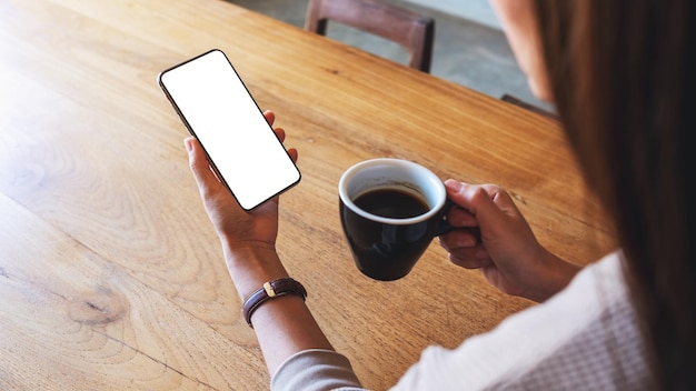 Mockup-afbeelding van een vrouw die een mobiele telefoon vasthoudt met een leeg wit desktopscherm terwijl ze koffie drinkt