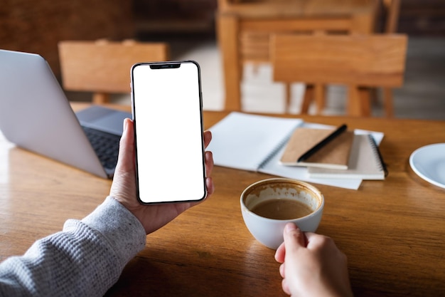 Mockup-afbeelding van een vrouw die een mobiele telefoon vasthoudt met een leeg wit desktopscherm terwijl ze koffie drinkt