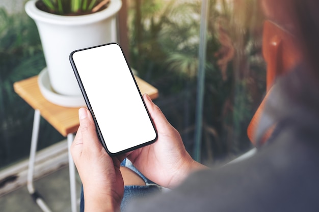 Mockup-afbeelding van een vrouw die een zwarte mobiele telefoon vasthoudt en gebruikt met een leeg desktopscherm in café