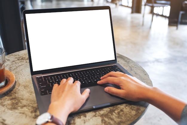 Mockup-afbeelding van een vrouw die gebruikt en typt op het toetsenbord van een laptopcomputer met een leeg wit desktopscherm in café