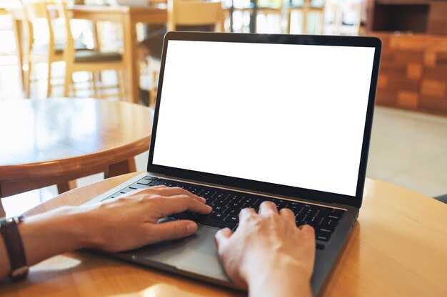 Mockup-afbeelding van een vrouw die gebruikt en typt op het toetsenbord van een laptopcomputer met een leeg wit desktopscherm op houten tafel