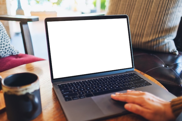 Mockup-afbeelding van een vrouw die het touchpad van een laptop gebruikt en aanraakt met een leeg wit desktopscherm op tafel