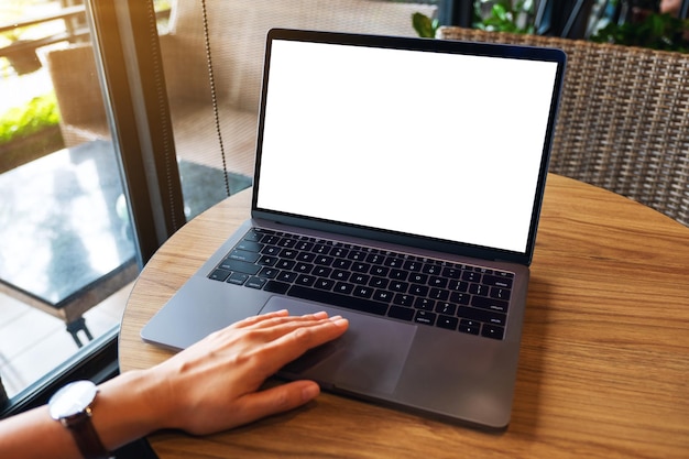 Mockup-afbeelding van een vrouw die het touchpad van een laptopcomputer gebruikt en aanraakt met een leeg wit desktopscherm op houten tafel