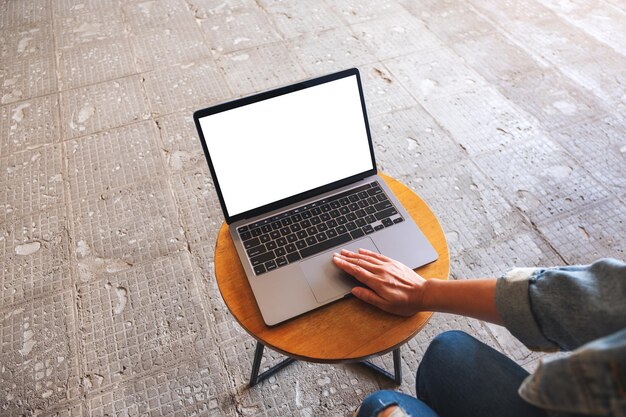 Mockup-afbeelding van een vrouw die het touchpad van een laptopcomputer gebruikt en aanraakt met een leeg wit desktopscherm op tafel