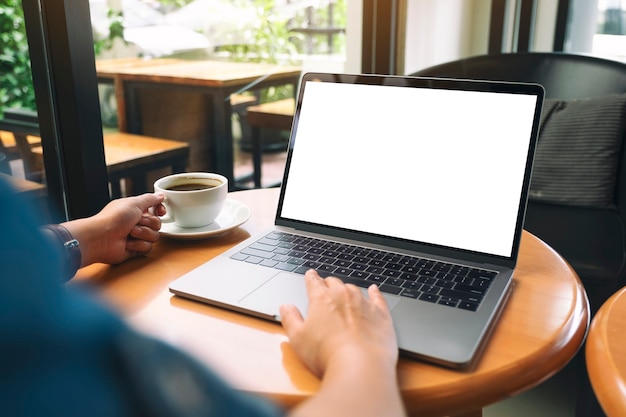 Mockup-afbeelding van een vrouw die laptop-touchpad gebruikt en aanraakt met een leeg wit bureaubladscherm terwijl ze koffie drinkt