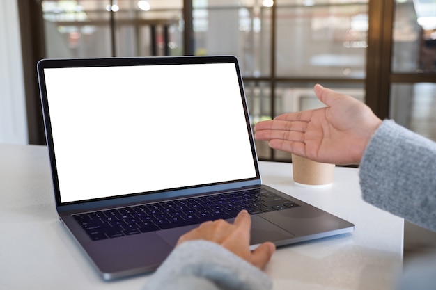 Mockup-afbeelding van een vrouw die met de hand wijst en het touchpad van een laptop aanraakt met een leeg wit desktopscherm op kantoor