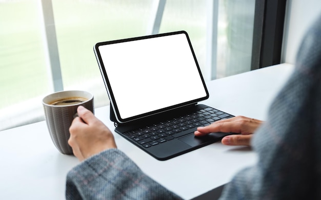 Mockup-afbeelding van een vrouw die tablet-touchpad gebruikt en aanraakt met een leeg wit bureaubladscherm als een computer-pc terwijl ze koffie drinkt