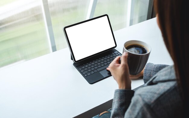 Mockup-afbeelding van een vrouw die tablet-touchpad gebruikt en aanraakt met een leeg wit bureaubladscherm als een computer-pc terwijl ze koffie drinkt