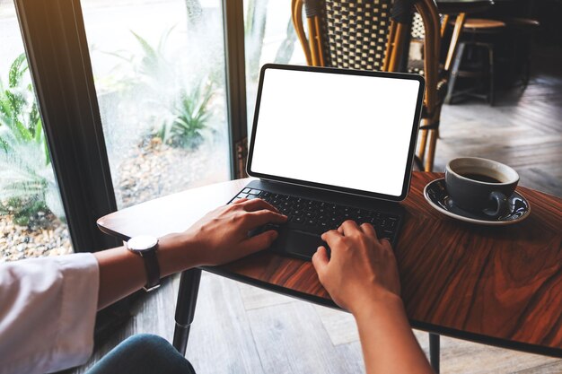 Mockup-afbeelding van een vrouw die typt op het toetsenbord van een tablet met een leeg wit bureaubladscherm als een computer-pc met een koffiekopje op tafel