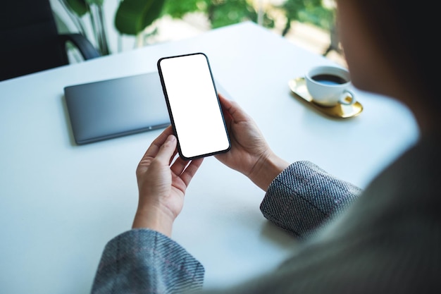 Mockup-afbeelding van een vrouw met een mobiele telefoon met een leeg wit desktopscherm met een laptop op tafel